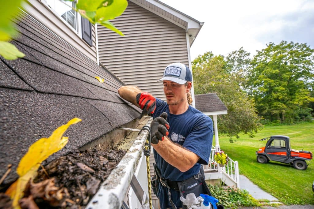 Gutter full of leaves, moss and debris being cleared by hand